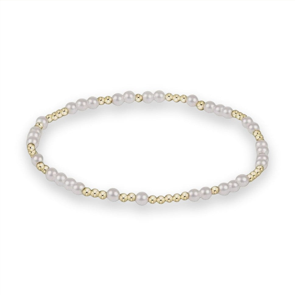 Fine jewelry bracelet by an unidentified designer centered on a neutral grey studio background featuring an alternating sequence of lustrous white pearls and polished gold-tone beads in a delicate circular arrangement