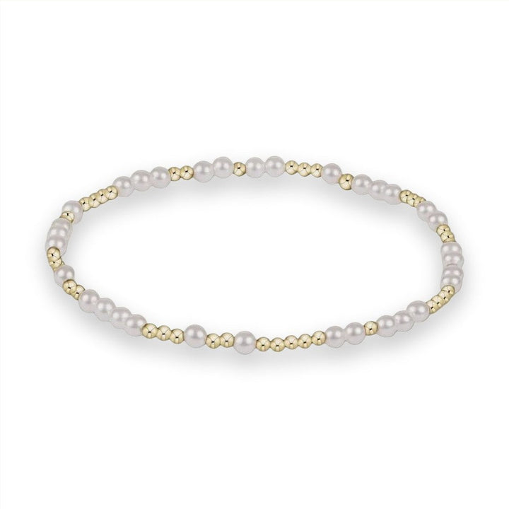 Fine jewelry bracelet by an unidentified designer centered on a neutral grey studio background featuring an alternating sequence of lustrous white pearls and polished gold-tone beads in a delicate circular arrangement
