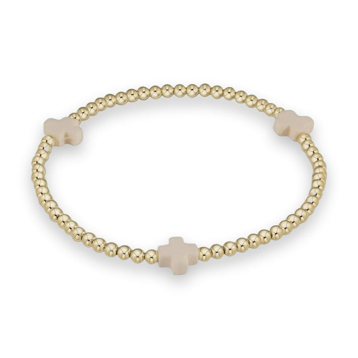 A gold beaded stretch bracelet with three cream-colored cross charms, displayed on a clean white background.