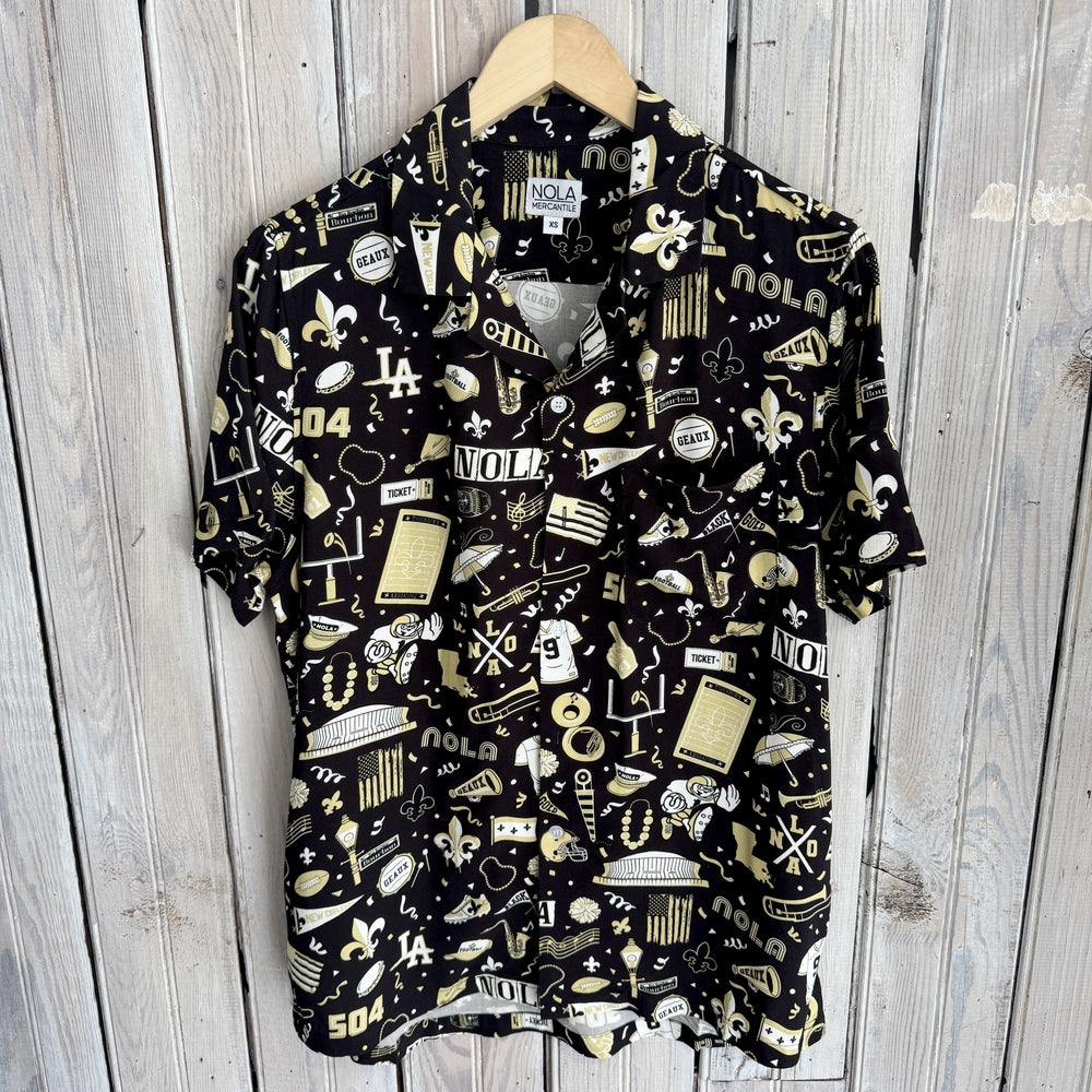 Black button-up shirt on a hanger with a gold and white NOLA print of fleur-de-lis, footballs and trumpets