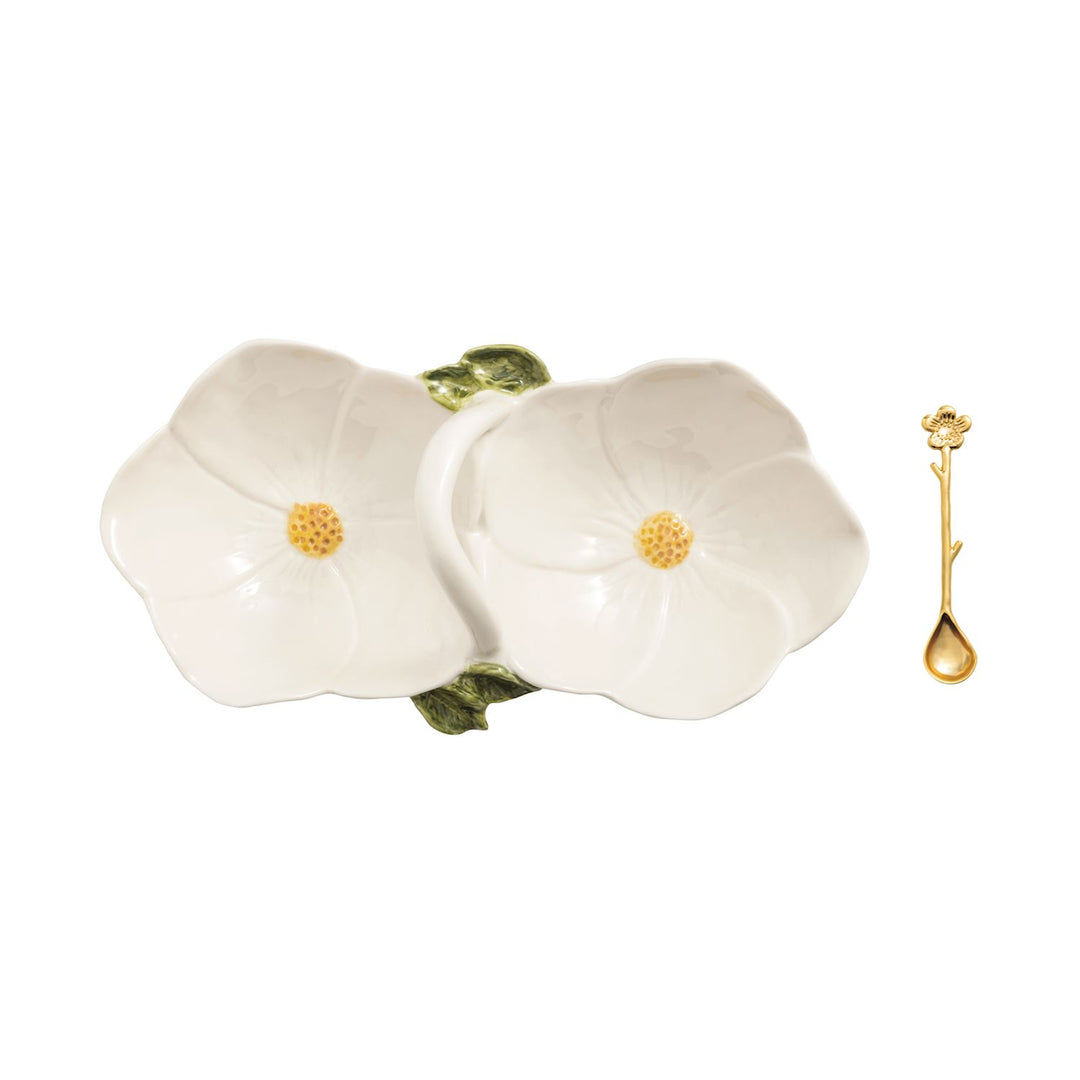 Hand-painted ceramic double-bowl condiment server designed as two white blossoms with textured yellow centers featuring green leaf accents and a small gold floral spoon on a plain white background