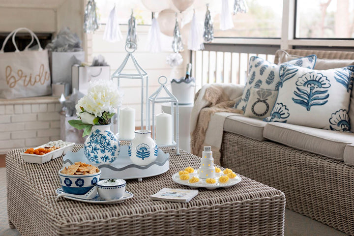 Photograph of a bridal celebration setup on a sunroom porch featuring blue and white floral ceramic vases, white metal lanterns, and a cream-colored bride tote bag in the background
