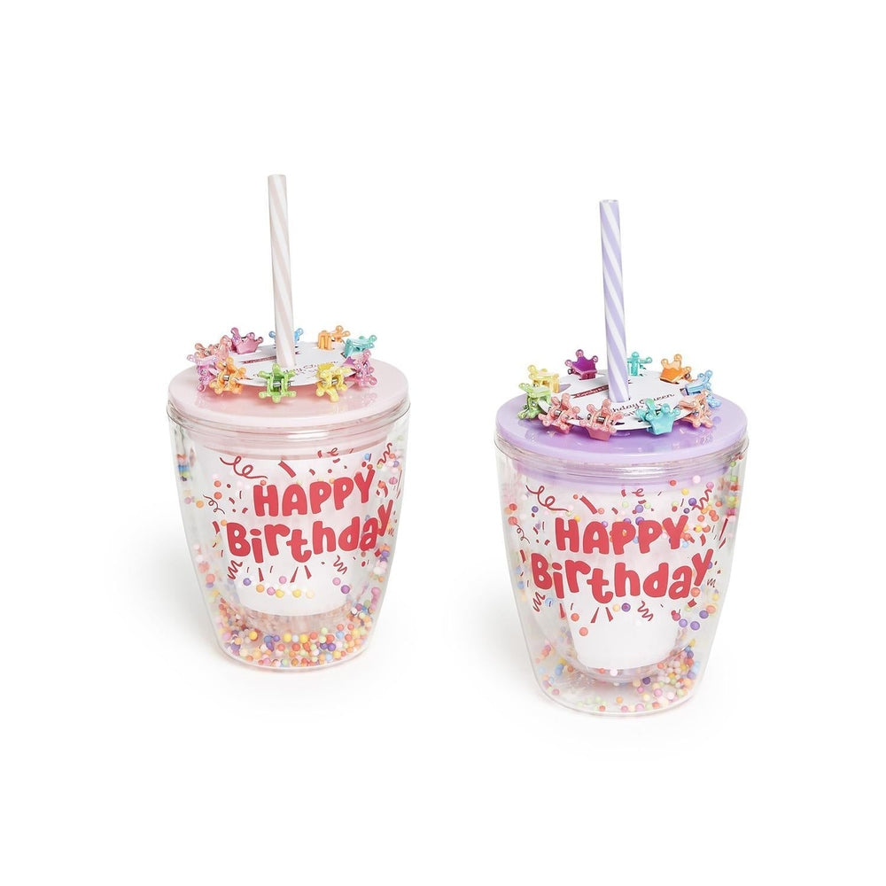 Product photograph of two plastic double-walled tumblers with pink and purple lids featuring Happy Birthday text in red bubble letters alongside colorful crown-shaped hair clips and confetti-filled bases against a white background