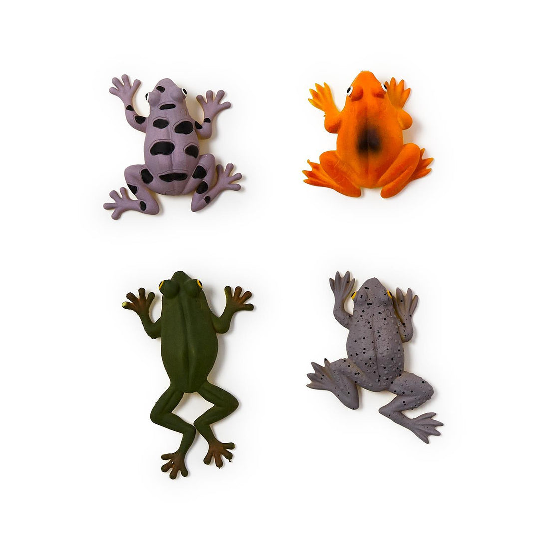 Molded plastic toy figurines of four colorful frogs on a white background featuring a purple frog with large black spots, a bright orange frog with a dark smudge, and a speckled grey frog