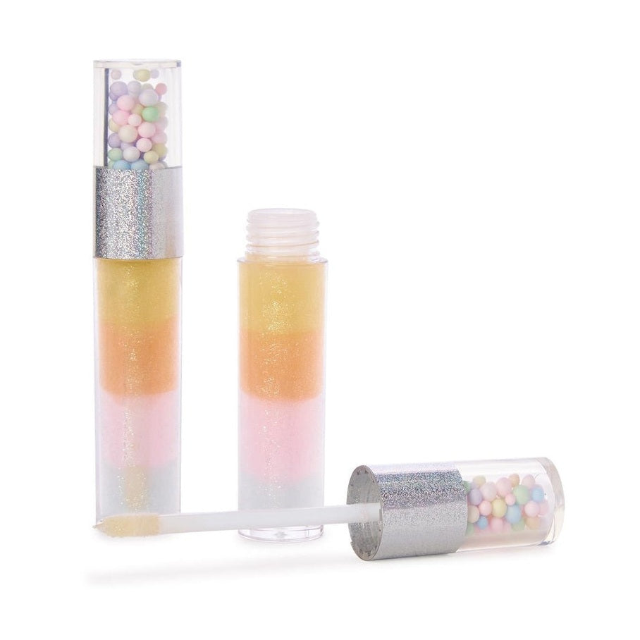 Studio product photograph of three layered lip gloss tubes on a white background featuring shimmering pastel gel segments and clear caps filled with tiny multicolored beads above a sparkling silver glitter band