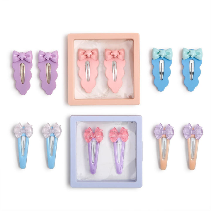 Product photograph of an assortment of pastel-colored snap hair clips arranged on a white background featuring scalloped edges, star-centered bows, and two pairs showcased in square peach and lavender display frames