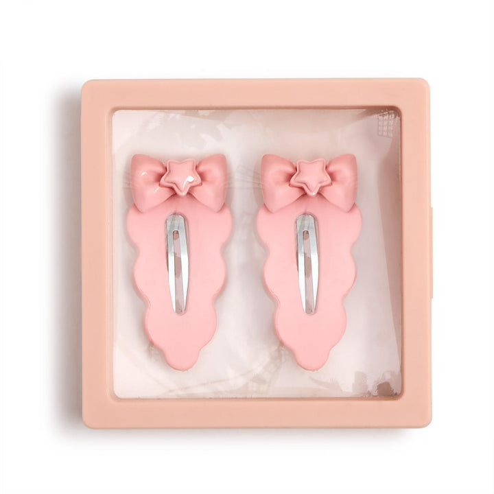 Plastic and metal hair accessories featuring two pink scalloped hair clips with star-embellished bows and silver snap fasteners inside a square pink display case on a white background