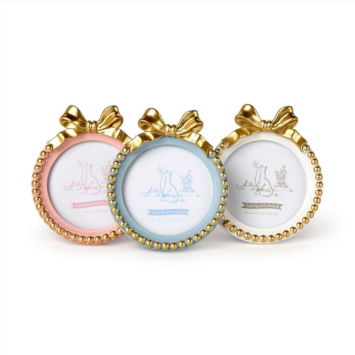 Resin photo frames by Cupcakes &amp; Cartwheels featuring three circular frames in pastel pink, blue, and cream topped with decorative gold bows and finished with metallic gold bead trim along the circular borders