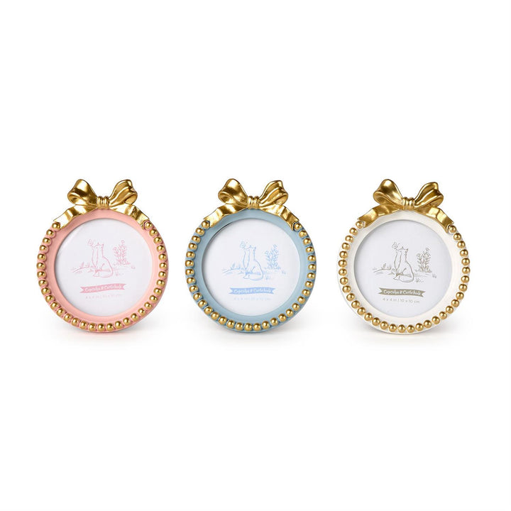 Resin decorative frames by Cupcakes &amp; Cartwheels featuring three small round photo frames in pastel pink, light blue, and cream white accented with ornate gold ribbon bows and beaded borders set against a plain white background