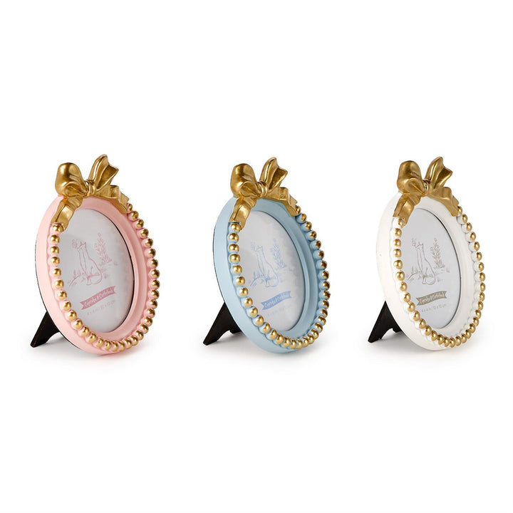 Three resin oval picture frames by Cupcakes &amp; Cartwheels displayed on a white background featuring pastel pink, blue, and white finishes with ornate gold bows and beaded borders