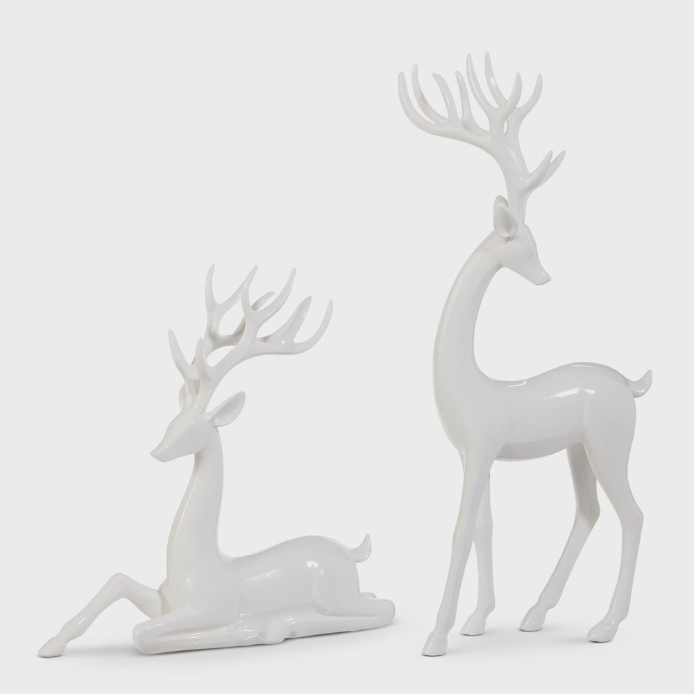 Two glossy white deer figurines with antlers, one lying down and one standing