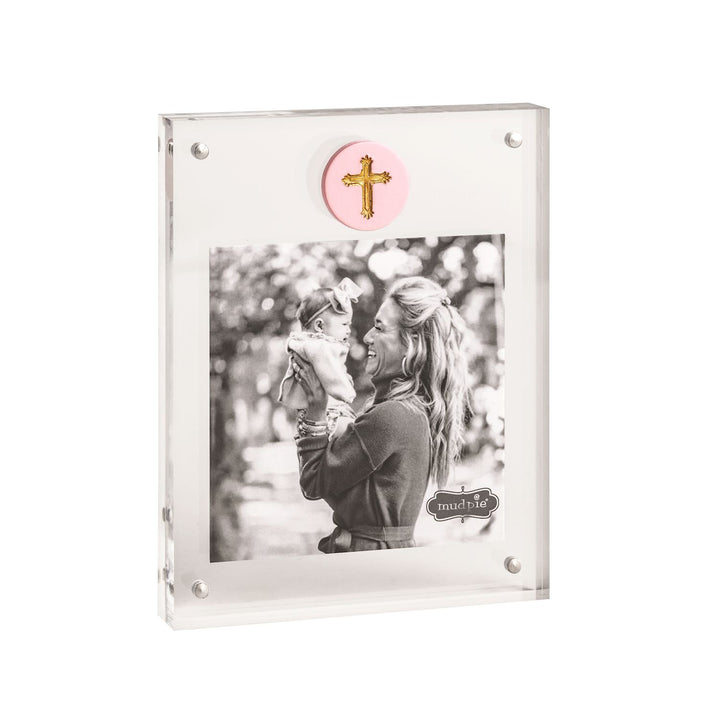 Acrylic magnetic picture frame by Mud Pie featuring a black and white photograph of a woman holding a baby in an outdoor garden setting with a pink ceramic medallion with a gold cross and silver magnetic corner fasteners