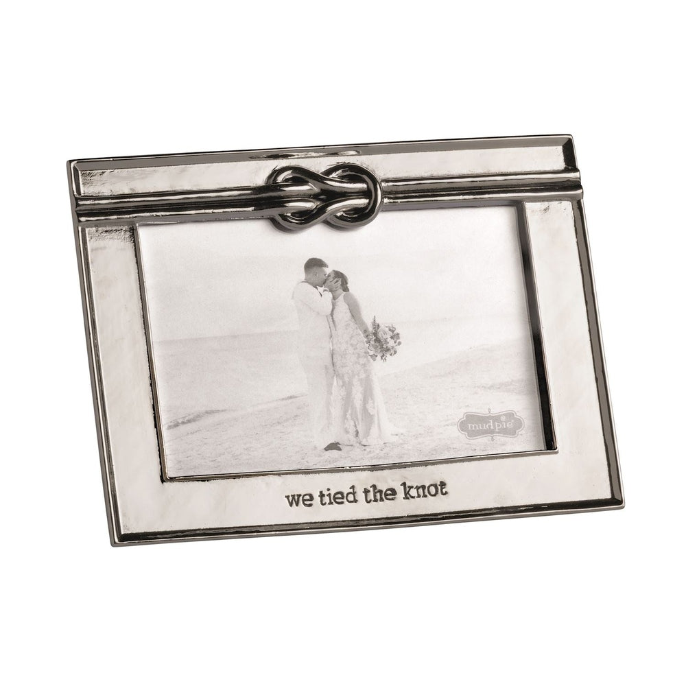 Cast metal frame by Mud Pie featuring a black and white photograph of a wedding couple kissing on a sandy beach shoreline with a decorative sculpted knot at the top and the engraved message we tied the knot at the base
