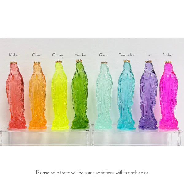 Translucent resin statues of the Virgin Mary are displayed in a colorful row on a clear acrylic shelf, featuring a spectrum of vibrant shades with each figure wearing a tiny gold crown and labeled with unique names like Matcha and Azalea