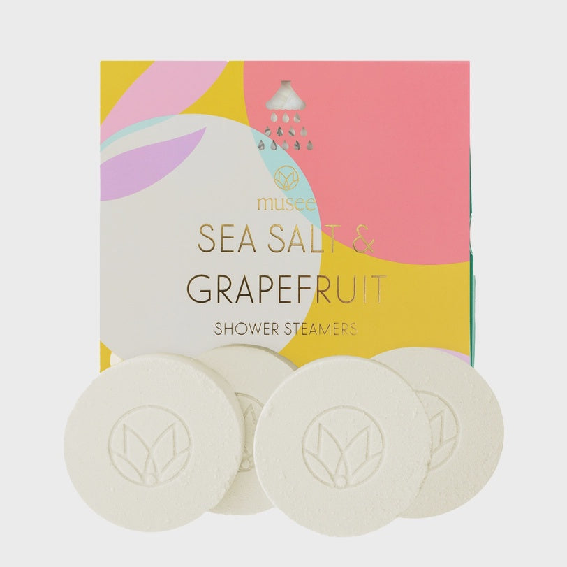 Product photograph of Musee Sea Salt and Grapefruit Shower Steamers displaying a box with abstract pink and yellow patterns, gold foil typography, and four white circular tablets embossed with a lotus logo