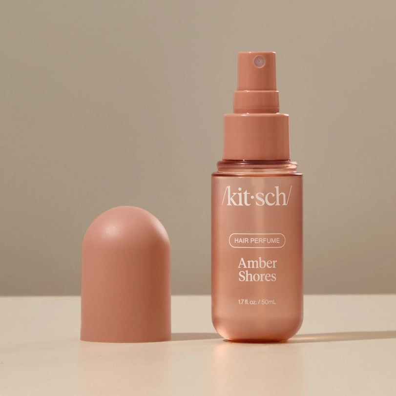 Digital product photography by Kitsch showcasing a metallic rose gold Amber Shores Hair Perfume bottle and matching rounded cap on a neutral surface with clean white brand lettering