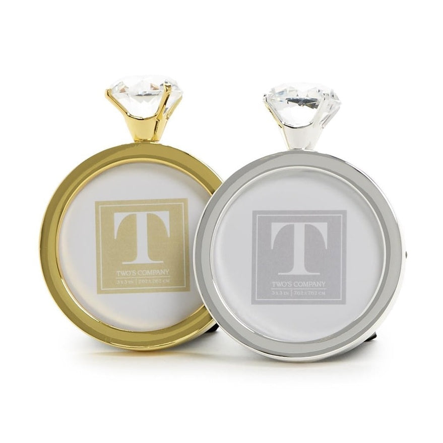 Product photography of Two's Company ring-shaped picture frames featuring a pair of gold and silver circular frames designed like oversized engagement rings with large faceted clear crystals and polished metallic finishes on a white studio background
