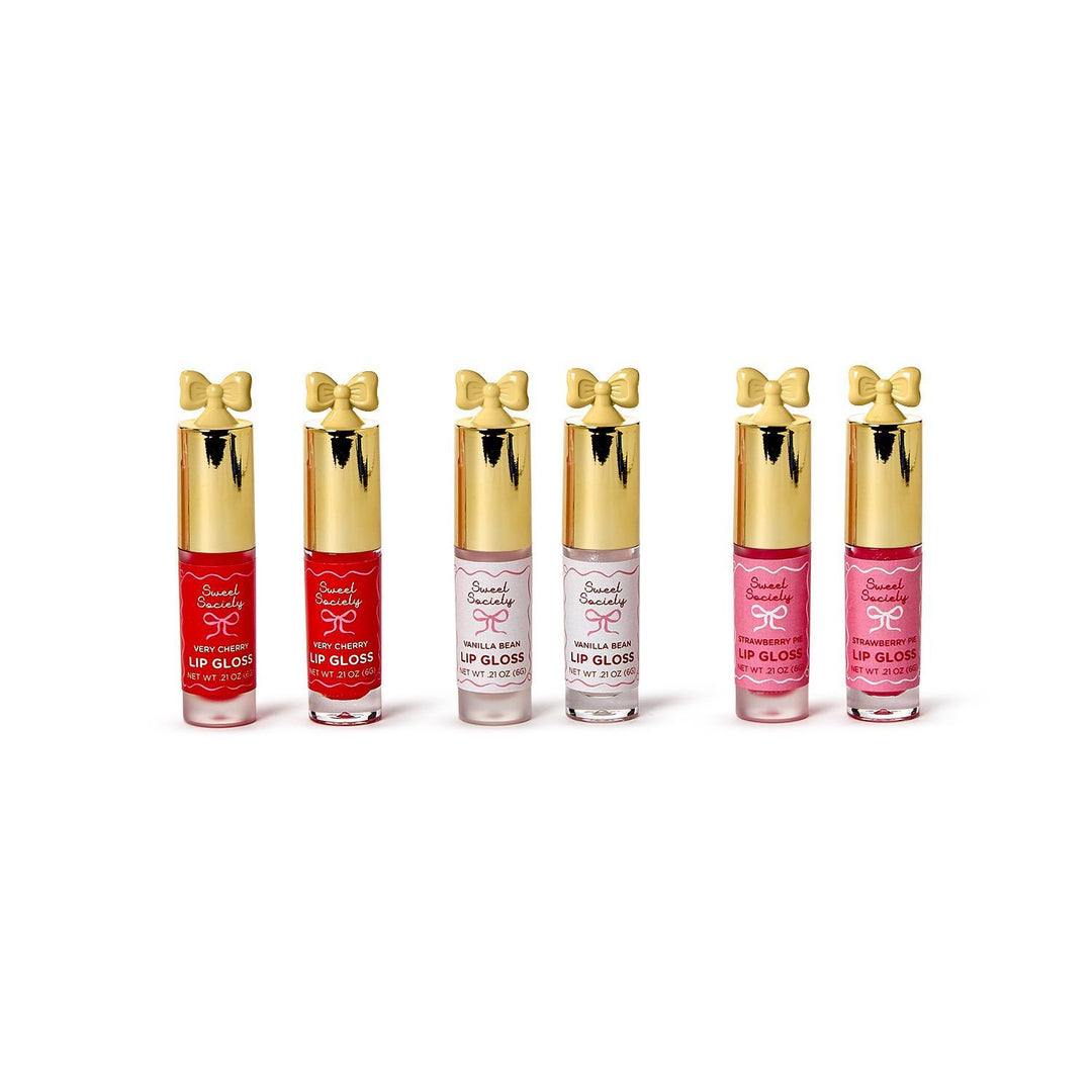 Studio product photograph of Sweet Society lip glosses on a white background showcasing six tubes with signature golden bow-shaped caps in Very Cherry red, translucent Vanilla Bean, and Strawberry Pie pink hues
