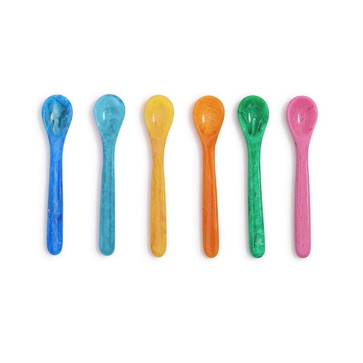 Hand-cast resin spoons by Dinosaur Designs arranged in a vertical row on a white background featuring translucent marbled swirls and a vibrant rainbow color palette of lapis, honey, and emerald hues