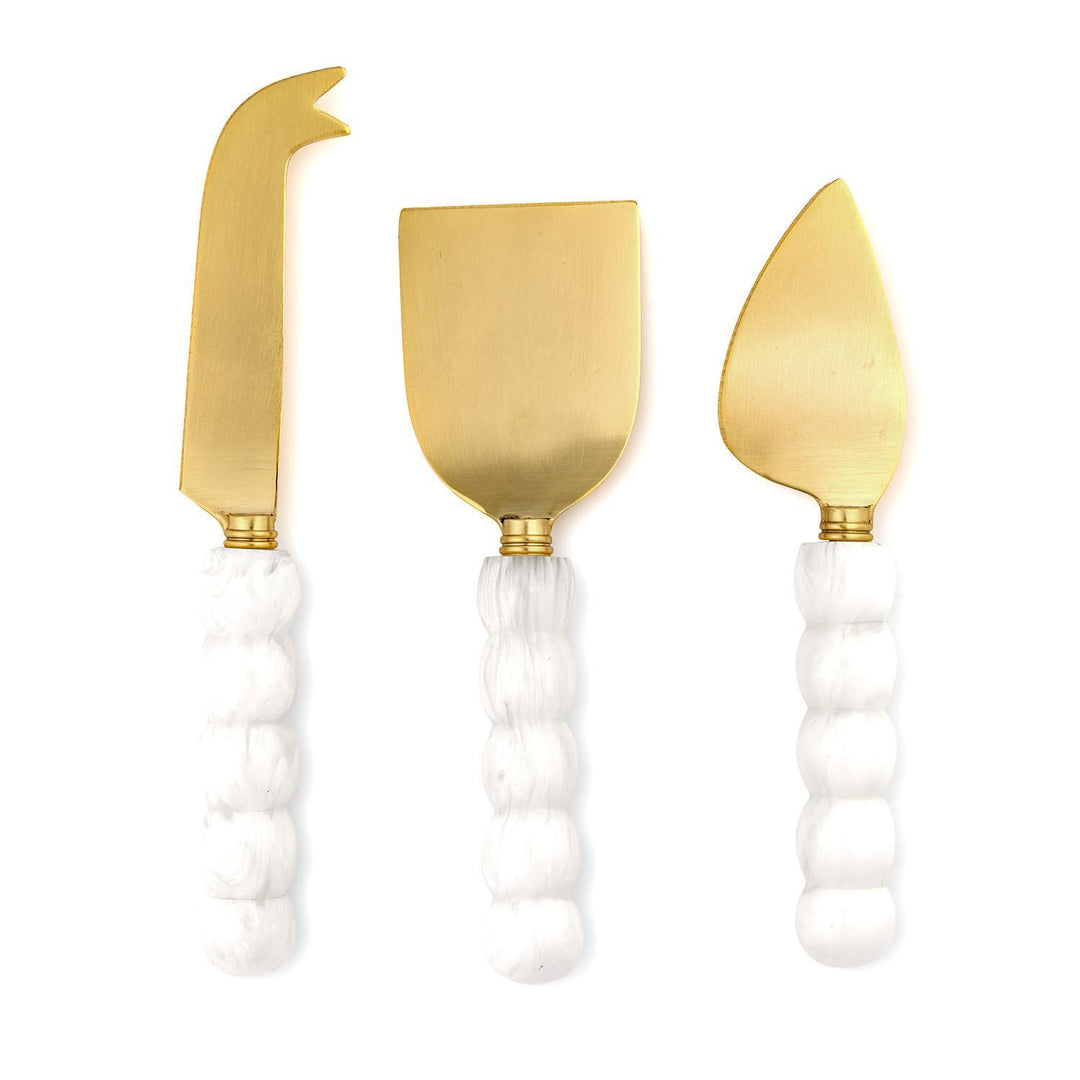 Gold-finished stainless steel three-piece cheese knife set featuring a flat spade, fork-tipped spear, and pointed almond knife with white marbled bobbin-style handles and a unique scalloped texture against a plain white background
