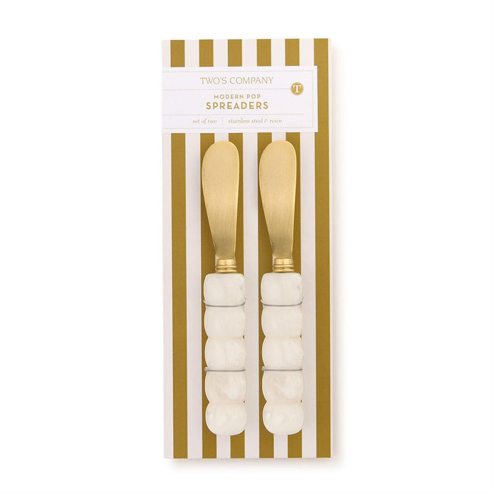 Two’s Company stainless steel and resin Modern Pop Spreaders featuring brushed gold-toned blades and white marbled bobble handles displayed on gold and white striped packaging with a circular T logo