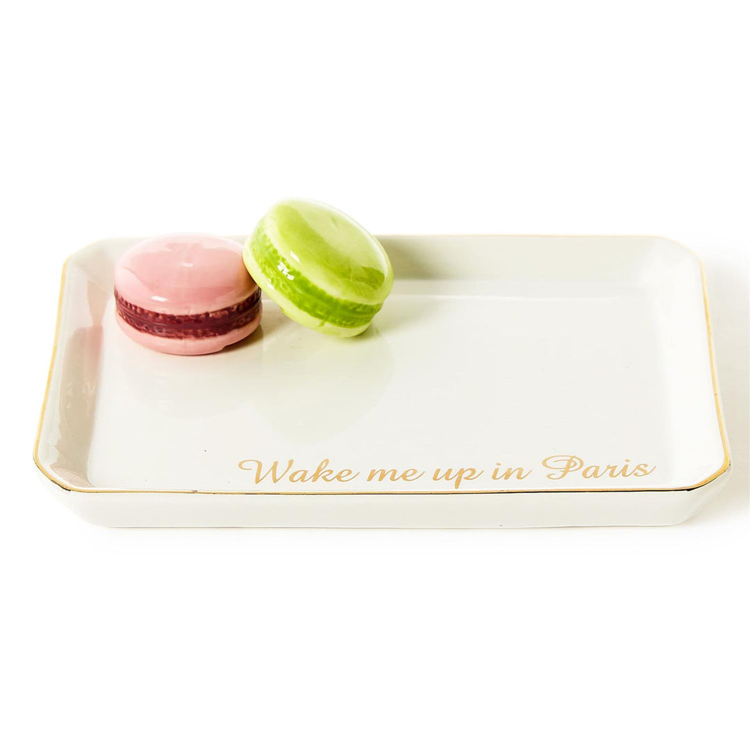 Ceramic trinket tray displaying a pink and lime green macaron with the gold cursive text Wake me up in Paris on a white rectangular surface finished with a gold-leaf rim