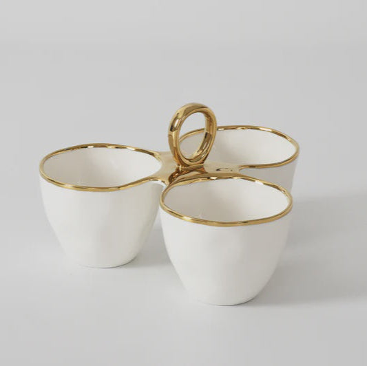 Ceramic three-compartment server featuring hand-formed white porcelain bowls with metallic gold rims and a central polished circular ring handle on a neutral studio background