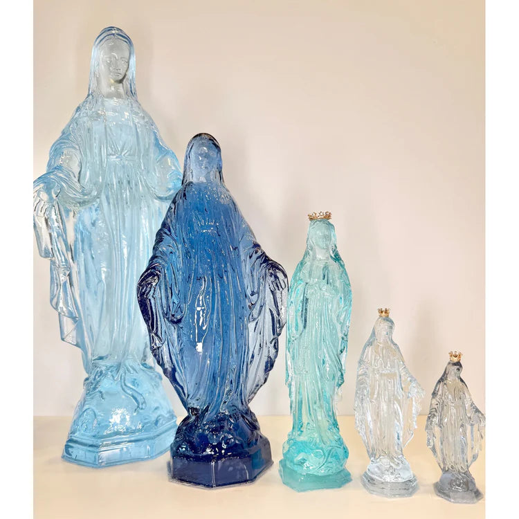 Translucent resin sculptures of the Virgin Mary standing in a row against a plain background featuring vibrant cobalt and seafoam green colors with tiny gold crowns on the smallest figures