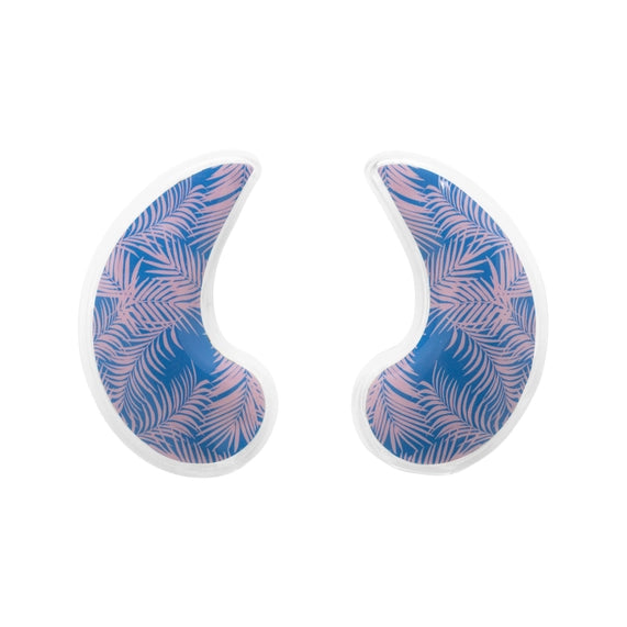 Digital product photography of two crescent-shaped gel cooling eye masks featuring a vibrant pink tropical palm leaf pattern on a navy blue background set against a minimalist white studio backdrop