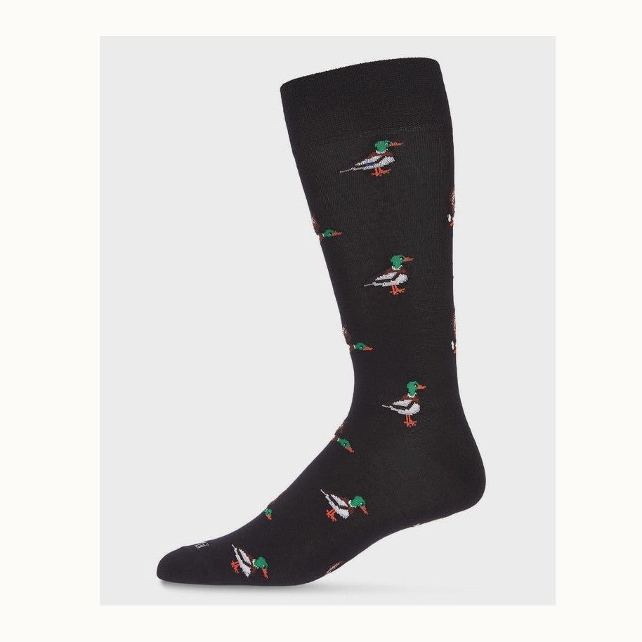 Knitted textile dress sock featuring a repeating pattern of miniature mallard ducks with vibrant emerald green heads and bright orange webbed feet against a solid black fabric and neutral studio background