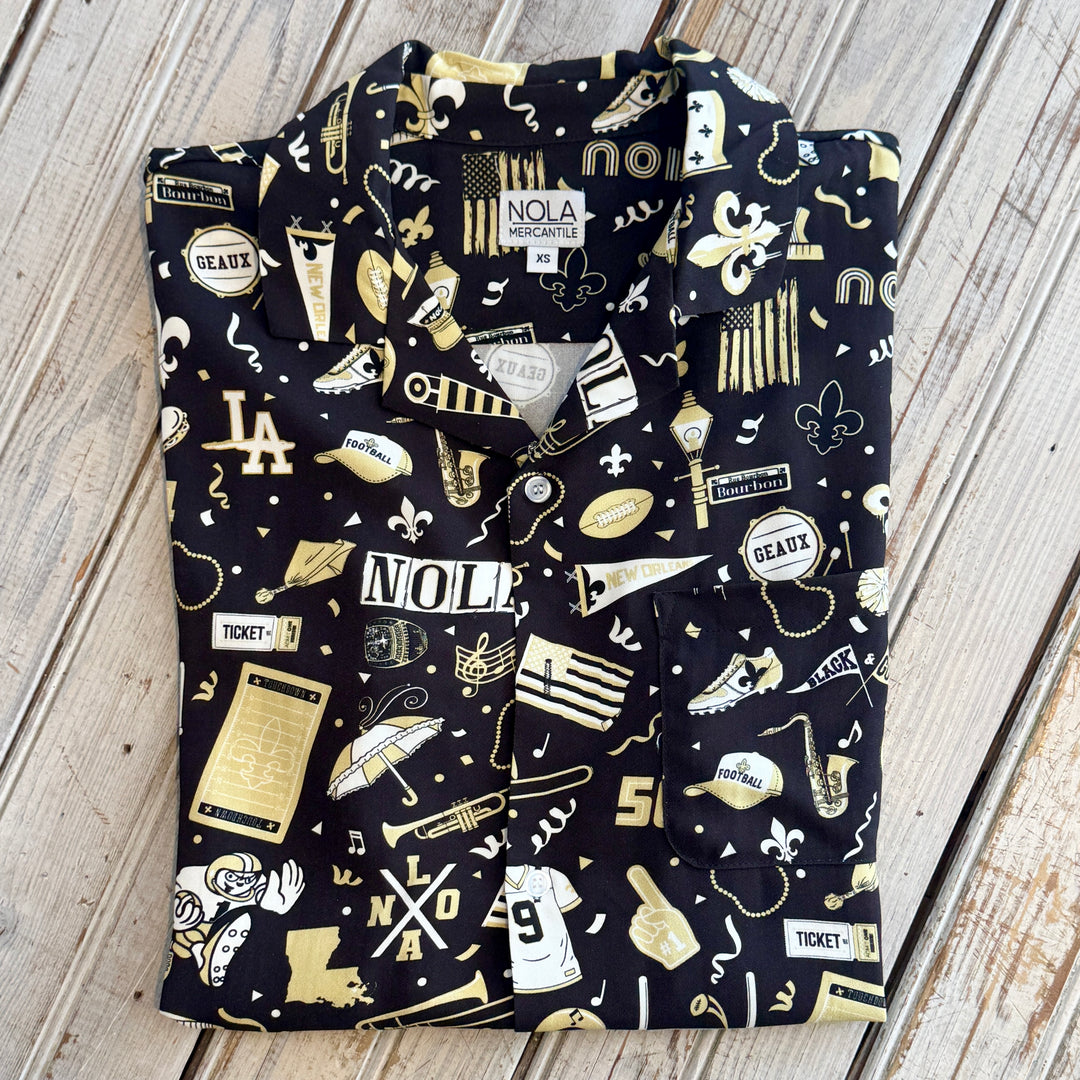Folded black button-up shirt with a gold and white NOLA football print and a NOLA Mercantile label