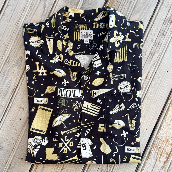 Folded black button-up shirt with a gold and white NOLA football print and a NOLA Mercantile label