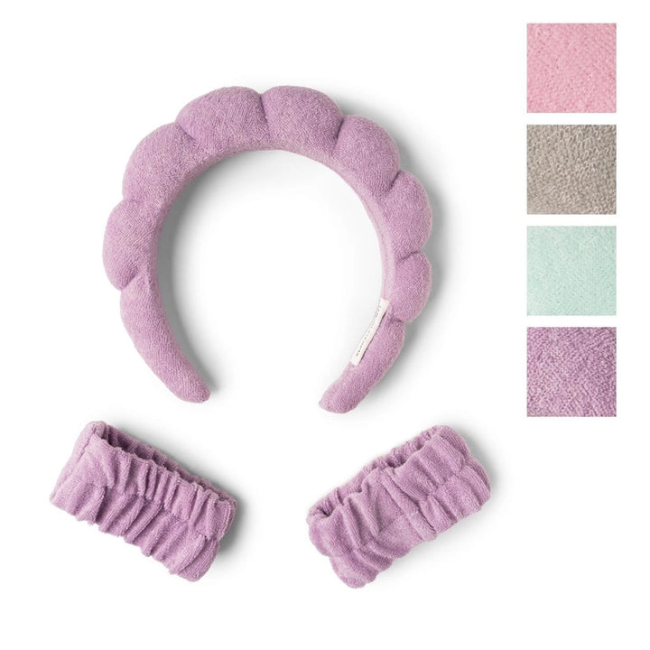 Product photograph of a lavender plush spa set featuring a padded bubble headband and two matching elastic wristbands displayed on a white background with additional color swatches in soft pink, taupe, and mint green