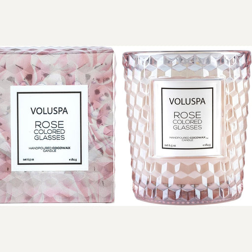 Product photograph by Voluspa of the Rose Colored Glasses candle and its matching gift box featuring a blush-toned honeycomb-textured glass jar, a geometric rose-patterned container, and elegant white labels with black typography