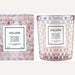 Product photograph by Voluspa of the Rose Colored Glasses candle and its matching gift box featuring a blush-toned honeycomb-textured glass jar, a geometric rose-patterned container, and elegant white labels with black typography