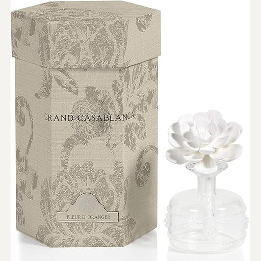 Commercial product photography of a Grand Casablanca Fleur d’Oranger room diffuser set featuring a beige hexagonal damask-patterned box and a clear glass bottle with a white multi-layered ceramic flower topper against a minimalist studio background