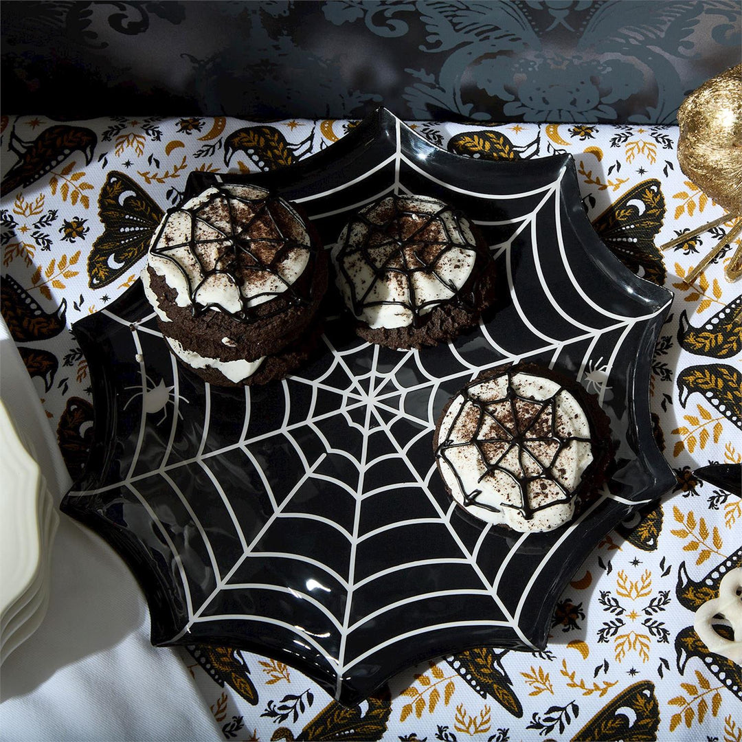 Black spiderweb plate holding chocolate sandwich cookies with web icing on a moth-print tablecloth
