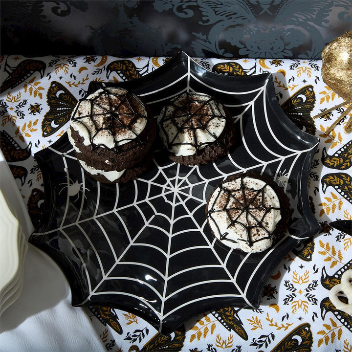 Black spiderweb plate holding chocolate sandwich cookies with web icing on a moth-print tablecloth
