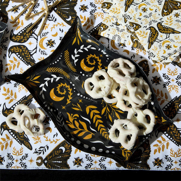 Black owl-shaped plate holding white yogurt-covered pretzels on a moth-print tablecloth