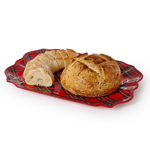 Product photograph of a golden-brown artisan round loaf and sliced baguette resting on a festive red Stewart tartan plaid platter with decorative scalloped edges against a plain white background