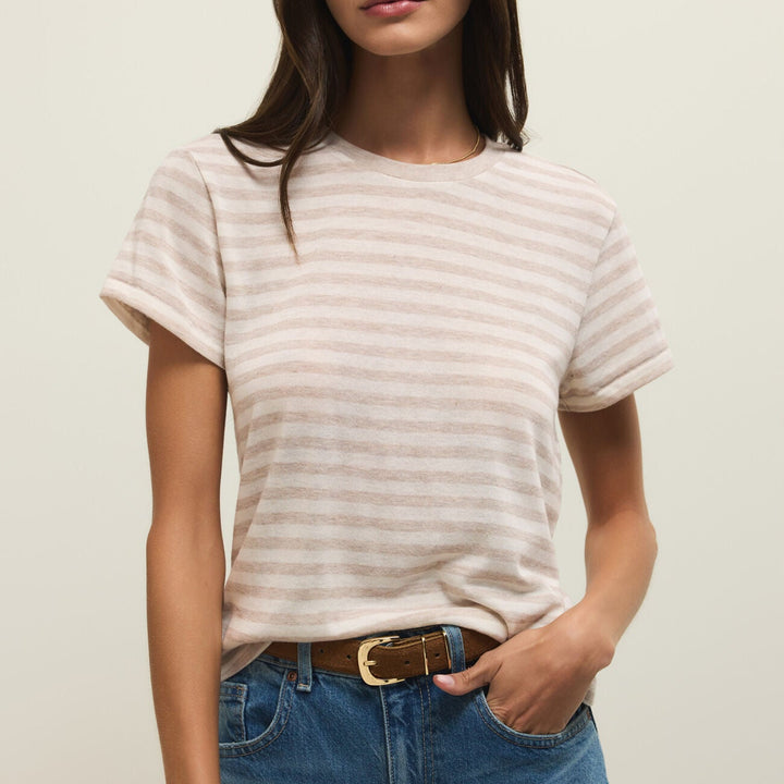 Studio photograph of a woman against a neutral background wearing a beige horizontal striped t-shirt with cuffed sleeves and blue jeans featuring a brown leather belt with a gold-tone buckle