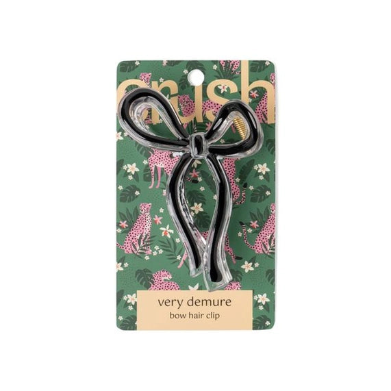 Product photography by Crush featuring a clear acrylic bow hair clip with a black ribbon core displayed on a green jungle-themed card with pink cheetahs and the phrase very demure bow hair clip