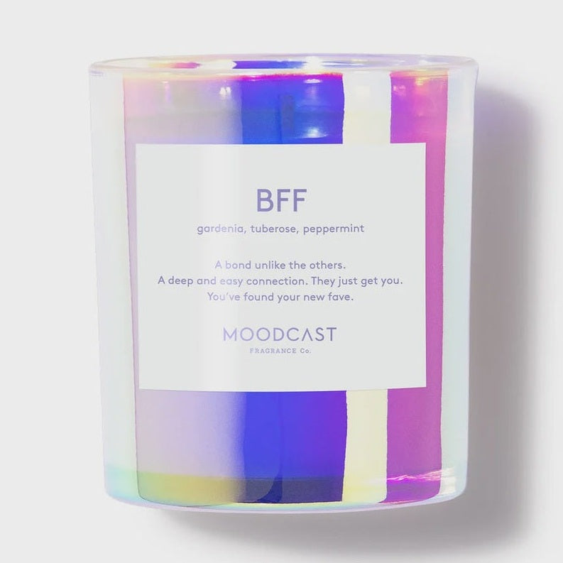 Product photography of a Moodcast Fragrance Co BFF scented candle centered on a neutral background, featuring an iridescent holographic glass vessel with vibrant purple reflections and a white minimalist label detailing notes of gardenia, tuberose, and peppermint
