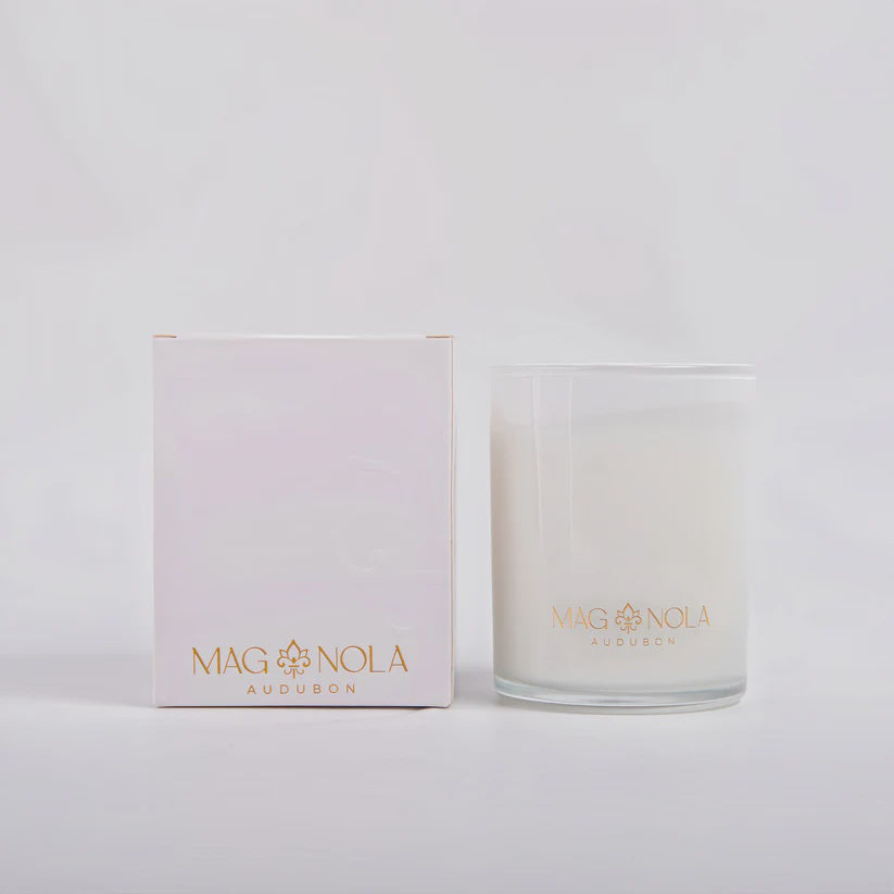 Product photography by MAGNOLA of an AUDUBON scented candle and matching white gift box in a minimalist studio setting featuring the iconic gold fleur-de-lis logo with white wax and clear glass details