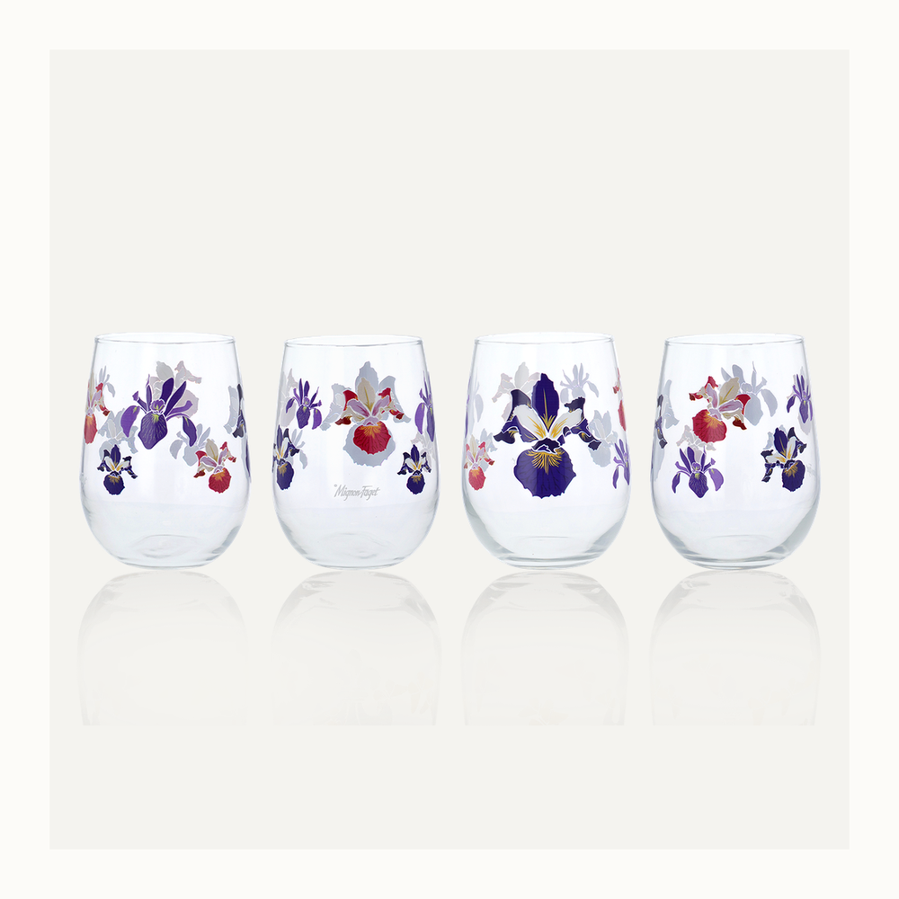 Stemless glassware by Mignon Faget featuring four clear wine glasses decorated with vibrant purple Louisiana irises and deep red floral accents on a reflective white surface