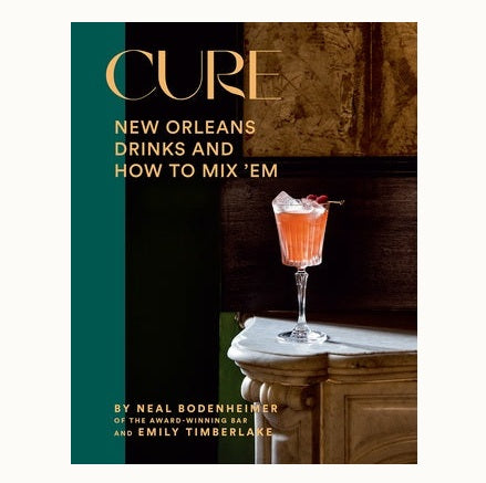 Book cover by Neal Bodenheimer and Emily Timberlake for Cure: New Orleans Drinks and How to Mix ‘Em featuring a vibrant orange cocktail in a fluted glass with fresh raspberries on a white marble mantelpiece