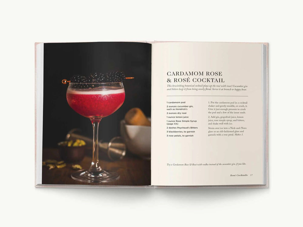 Photograph from the Rosé Cocktails cookbook featuring a vibrant pink Cardamom Rose and Rosé cocktail in a gold-rimmed glass garnished with skewered blackberries and a frothy foam head next to its printed recipe page