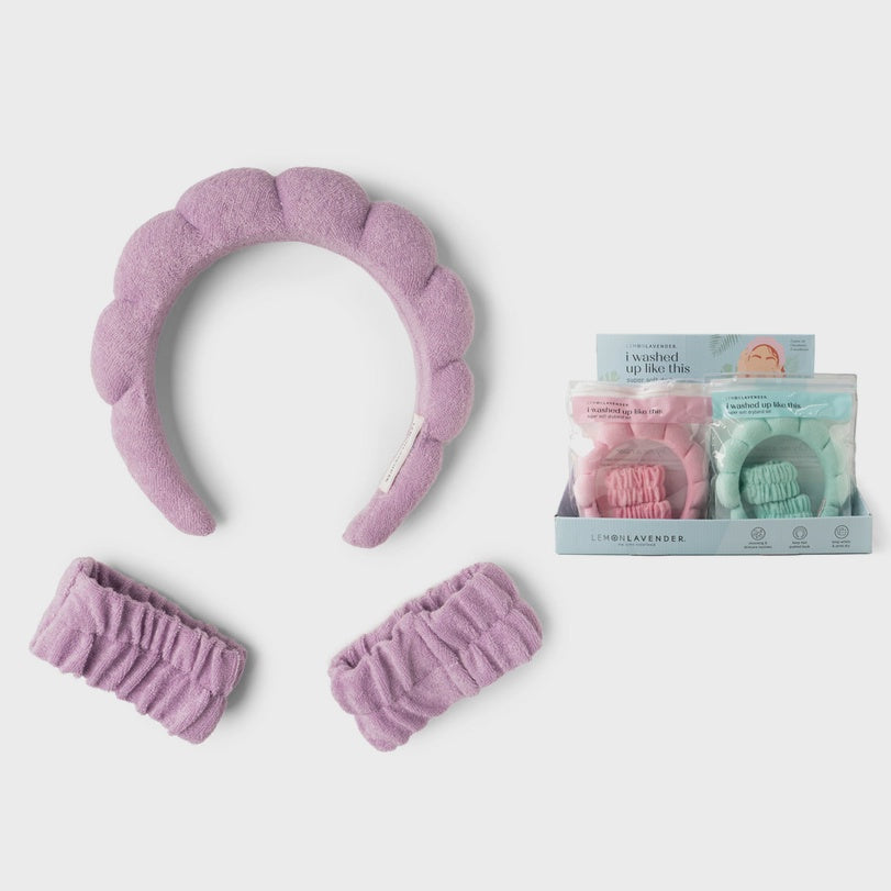 Commercial product photograph by Lemon Lavender of a lavender purple plush spa headband and matching wristbands on a neutral background with a retail display box highlighting puffy scalloped textures and soft terry cloth in pink and mint green