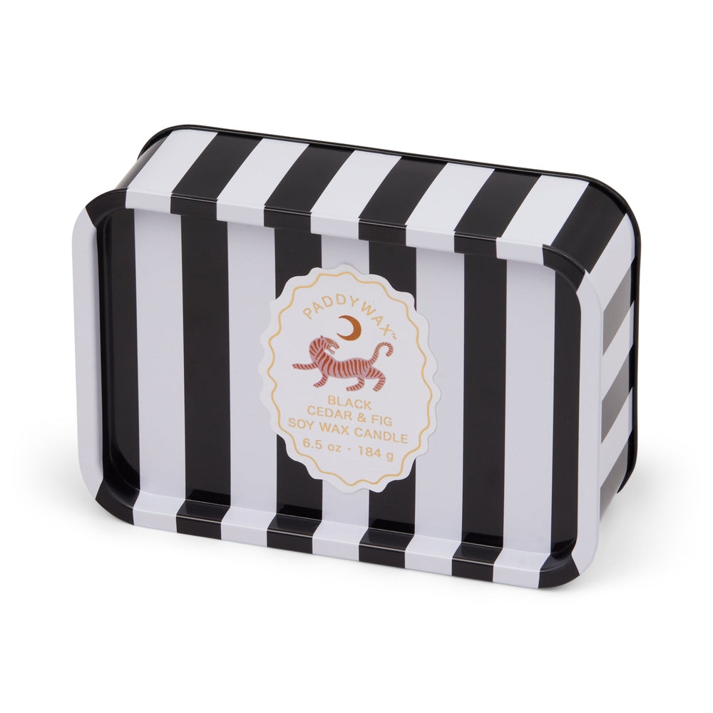 Tin soy wax candle by Paddywax featuring a rectangular container with bold black and white vertical stripes and a decorative scalloped label depicting a red tiger illustration for the Black Cedar and Fig scent