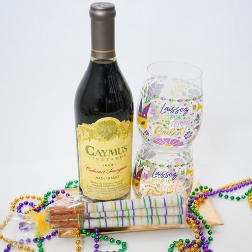 Bottle of Caymus wine, bottle of water, and Mardi Gras beads on a white background